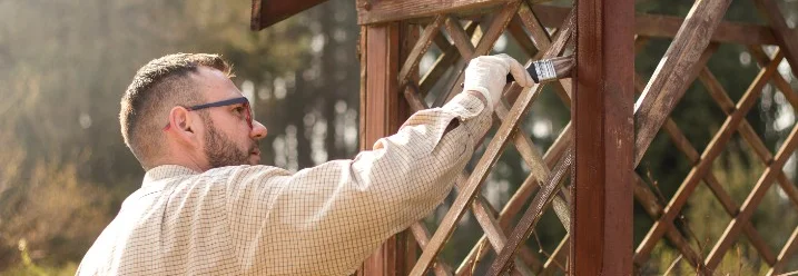 Person streicht Gartenlaube mit Pinsel